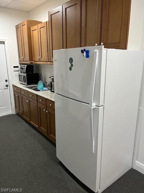 Kitchen featuring freestanding refrigerator, dark colored carpet, stainless steel microwave, and brown cabinets
