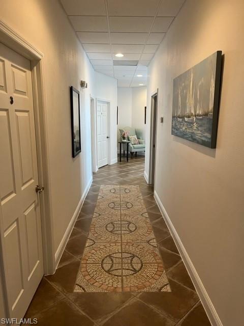 Hallway featuring dark tile patterned floors and a paneled ceiling
