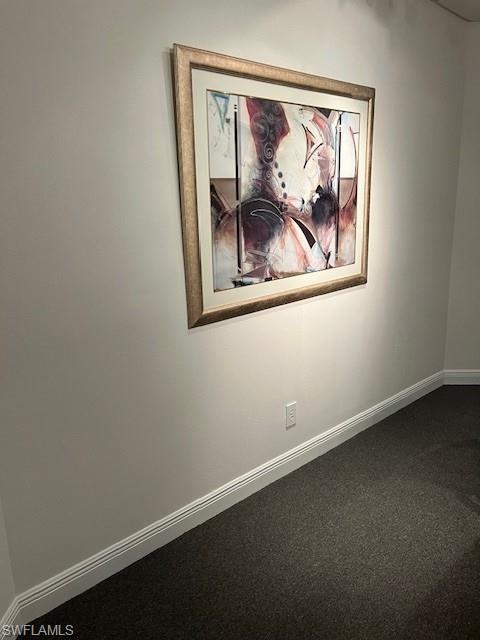 Empty room featuring baseboards and dark carpet