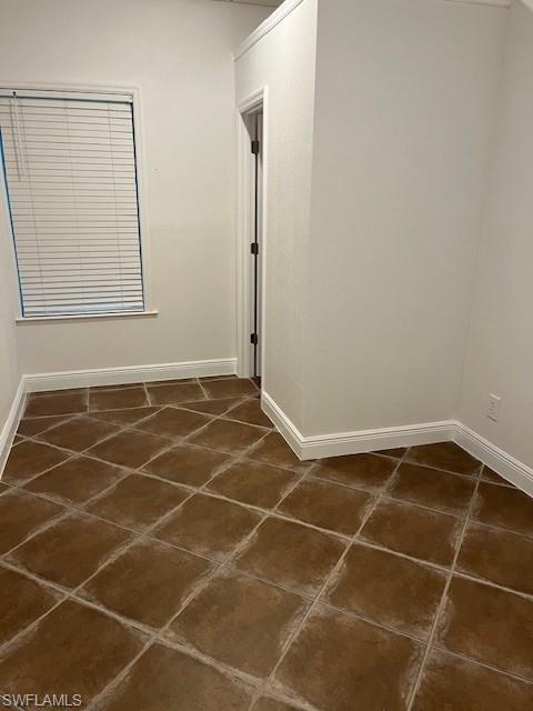 Spare room featuring baseboards and dark tile patterned floors