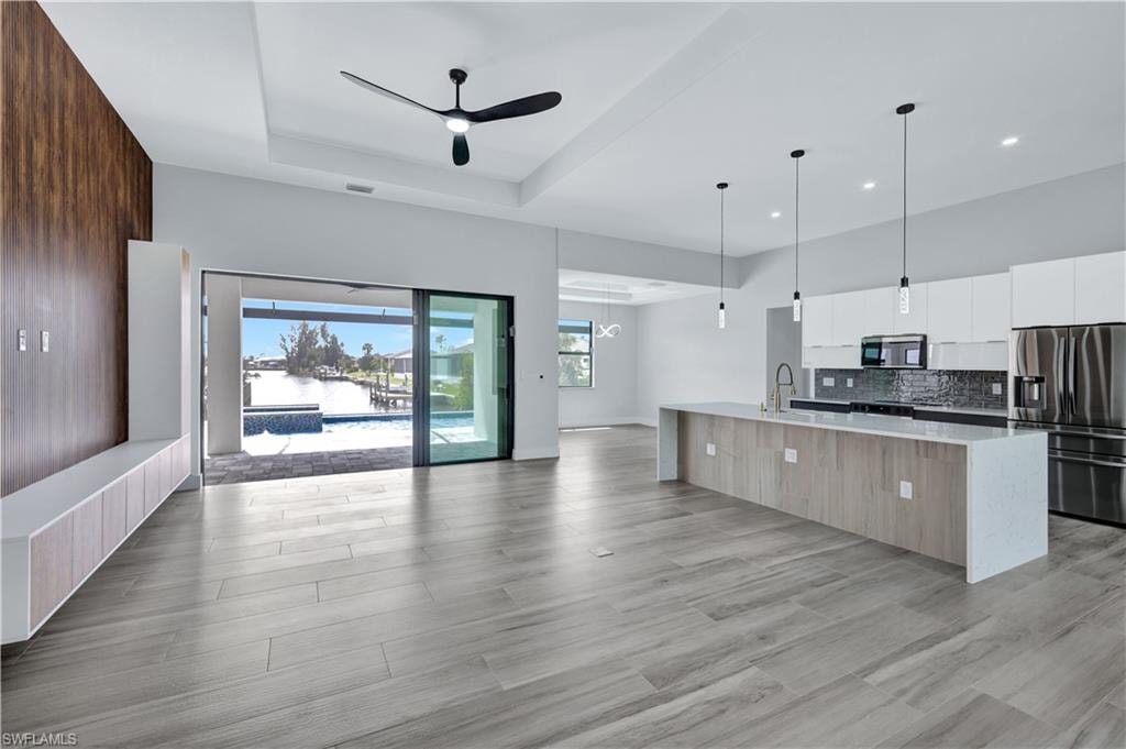 Kitchen with open floor plan, a raised ceiling, ceiling fan, modern cabinets, and appliances with stainless steel finishes