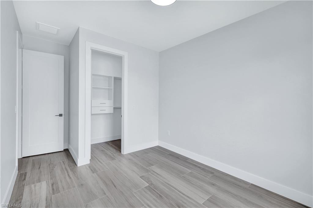 Unfurnished bedroom with a closet, visible vents, baseboards, wood finished floors, and attic access