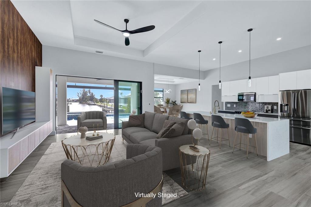 Living room featuring a ceiling fan, light wood-style flooring, recessed lighting, a tray ceiling, and a towering ceiling