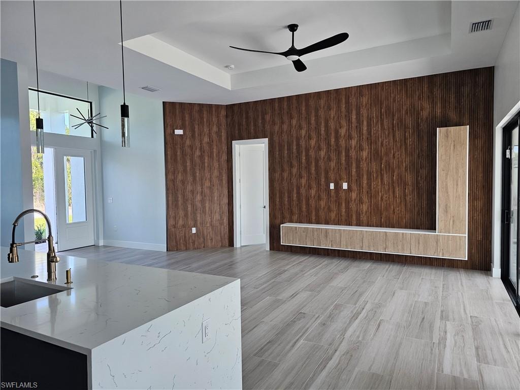 Living room featuring ceiling fan, wood walls, visible vents, light wood-type flooring, and a raised ceiling