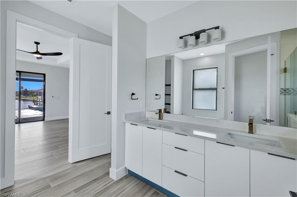 Full bath with double vanity, ceiling fan, a sink, and wood finished floors