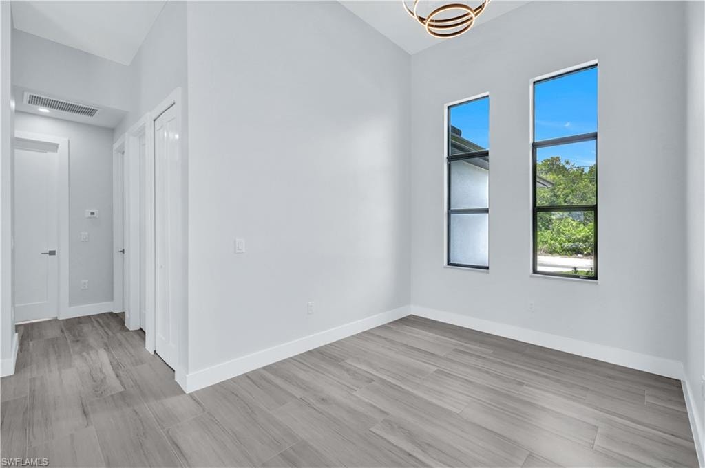 Empty room featuring baseboards, visible vents, light wood-type flooring, and a notable chandelier