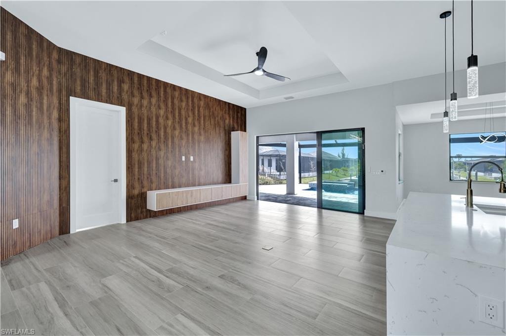 Unfurnished living room featuring a sink, a tray ceiling, wooden walls, and ceiling fan
