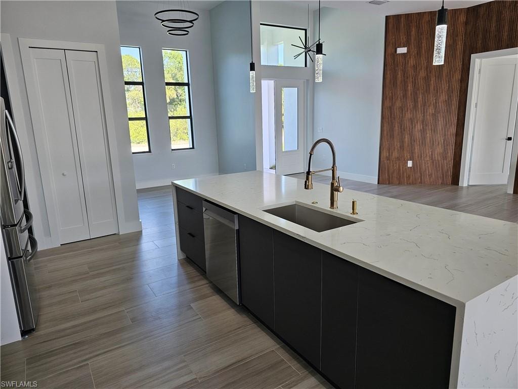 Kitchen featuring light wood-style flooring, a sink, hanging light fixtures, appliances with stainless steel finishes, and dark cabinetry