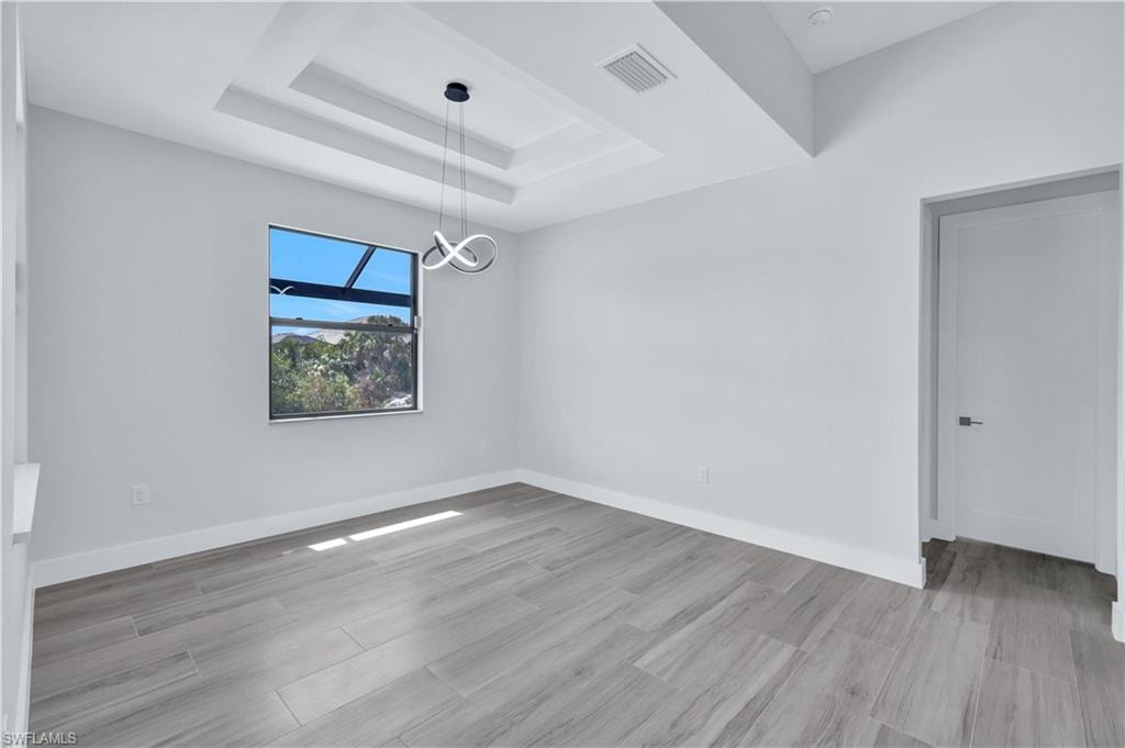 Empty room featuring a tray ceiling, wood finished floors, baseboards, visible vents, and an inviting chandelier