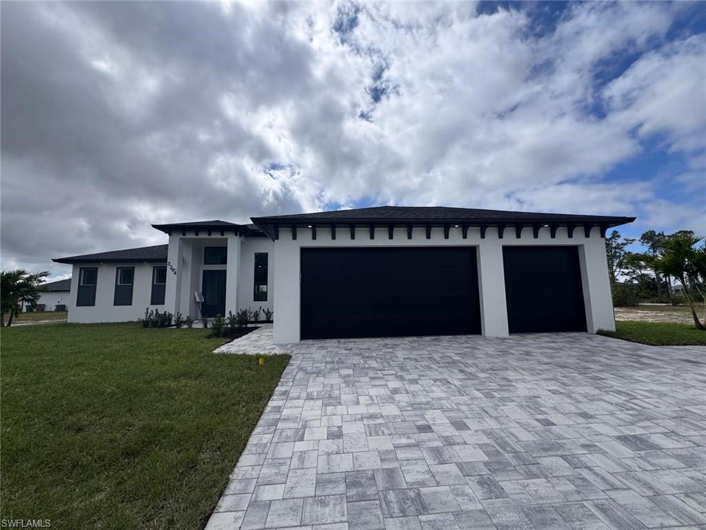 View of front of house featuring a garage, stucco siding, decorative driveway, and a front yard