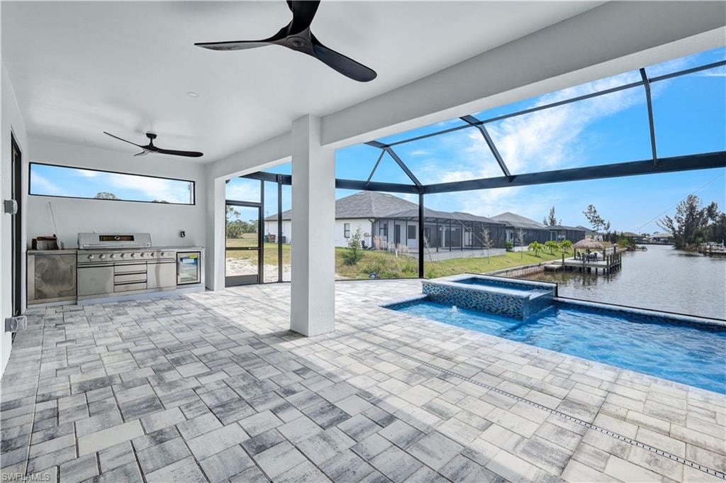 View of pool featuring a water view, exterior kitchen, glass enclosure, a patio, and ceiling fan