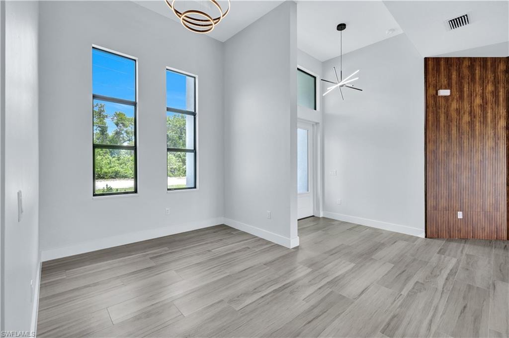 Unfurnished room featuring light wood-style flooring, visible vents, baseboards, a high ceiling, and an inviting chandelier