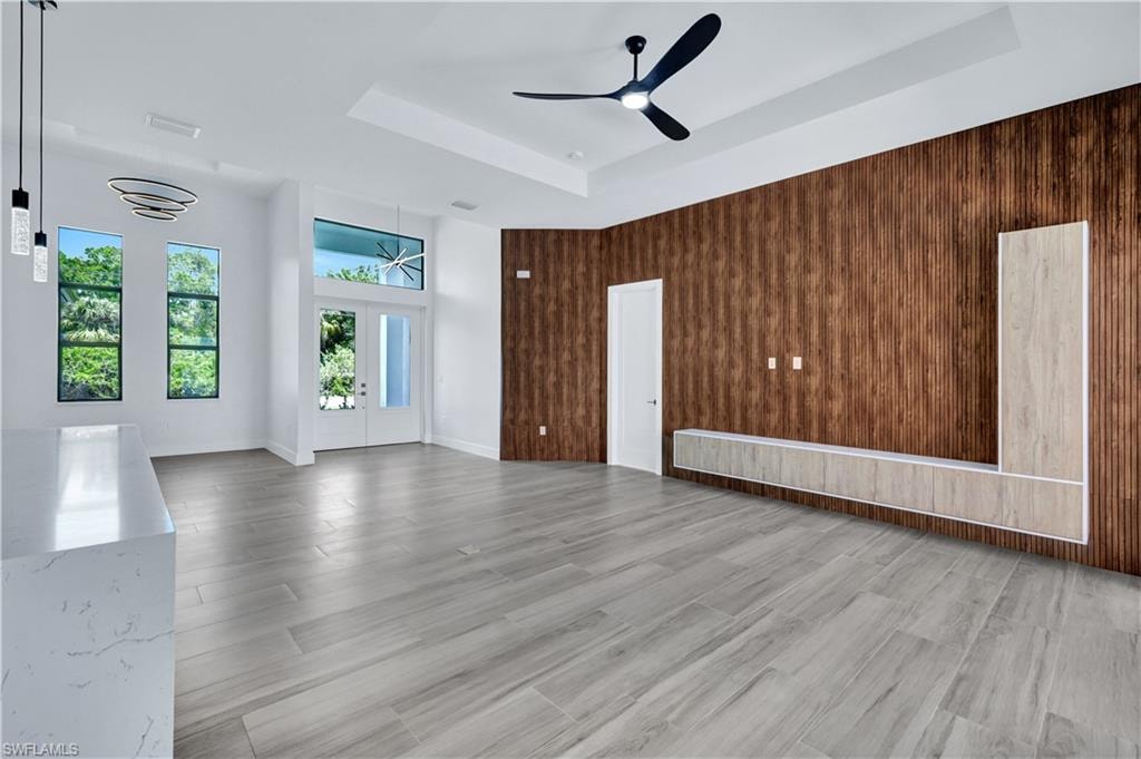Empty room featuring wooden walls, a ceiling fan, light wood-style floors, and a raised ceiling