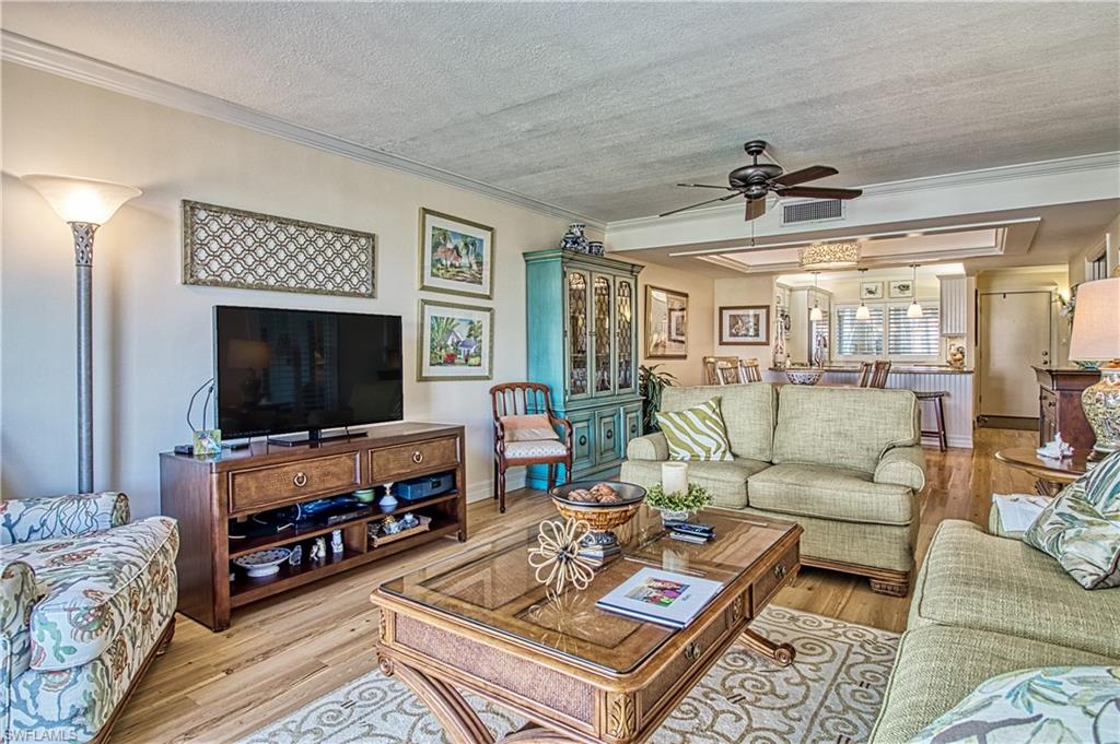 Kitchen with white cabinets, light stone countertops, pendant lighting, ornamental molding, and light wood-style floors