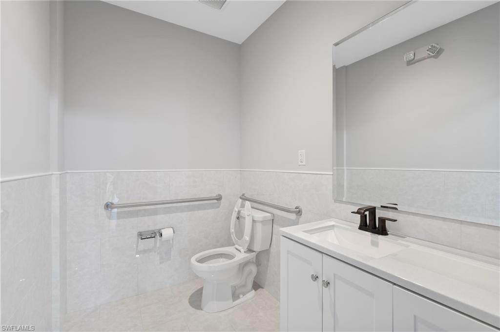 Half bath with vanity, tile walls, a wainscoted wall, and light tile patterned flooring