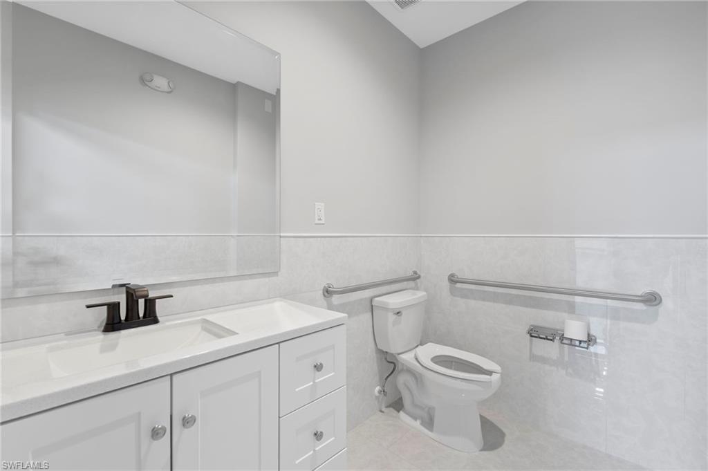 Bathroom with tile walls, vanity, a wainscoted wall, and light tile patterned floors