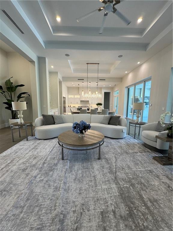 Living area with a tray ceiling, recessed lighting, ceiling fan with notable chandelier, and visible vents