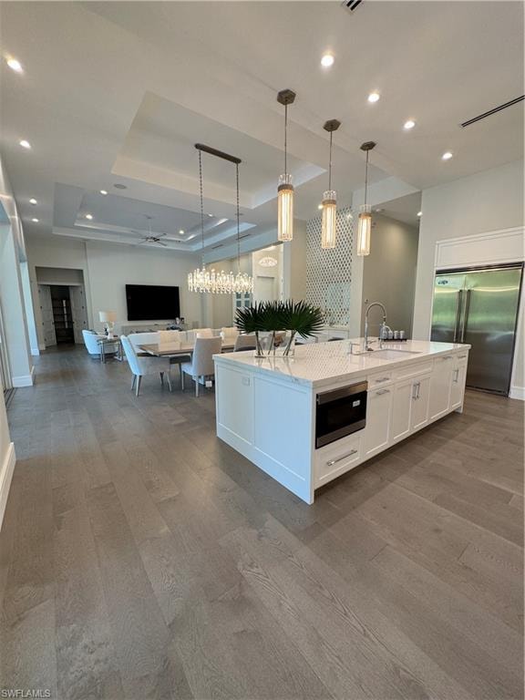 Kitchen featuring open floor plan, fridge, white cabinetry, a raised ceiling, and a kitchen island with sink