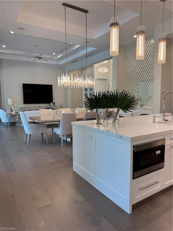 Kitchen with a sink, a tray ceiling, decorative light fixtures, and white cabinetry