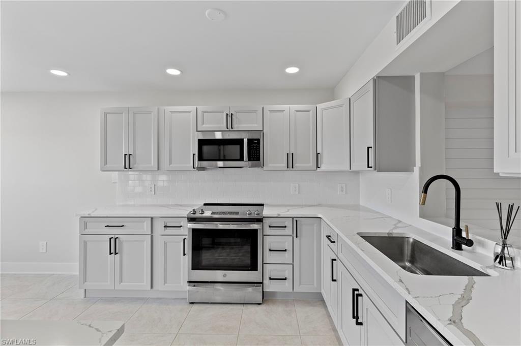 Kitchen featuring sink, light stone countertops, light tile patterned floors, and stainless steel appliances