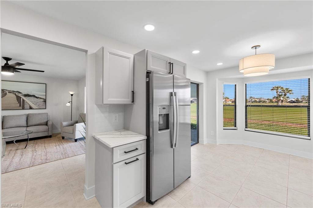 Kitchen with ceiling fan, hanging light fixtures, light stone countertops, stainless steel fridge, and light tile patterned floors