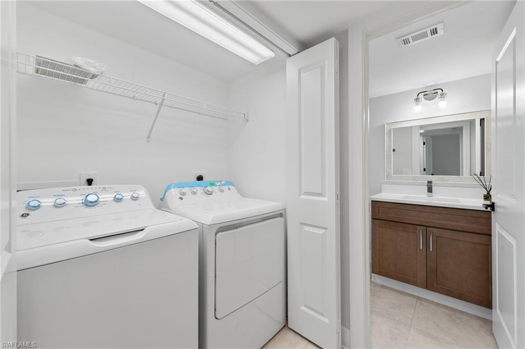 Clothes washing area featuring light tile patterned flooring, washer and clothes dryer, and sink