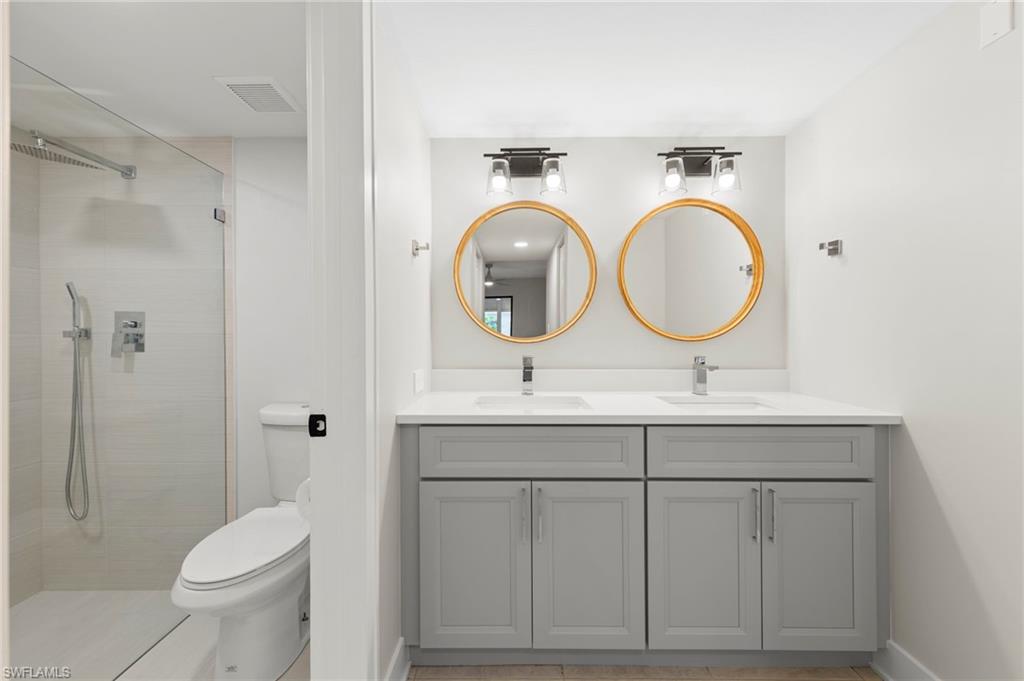 Bathroom with dual vanity, toilet, a tile shower, and tile patterned flooring