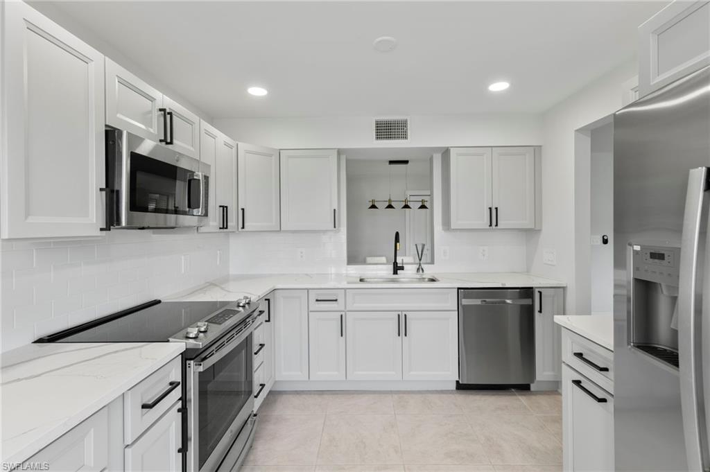 Kitchen featuring light tile patterned flooring, backsplash, light stone countertops, appliances with stainless steel finishes, and sink