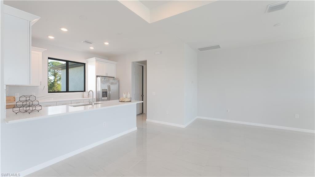 Kitchen featuring white cabinets, stainless steel fridge, light tile patterned floors, and sink