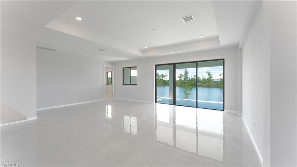 Unfurnished room with light tile patterned floors, a tray ceiling, and a water view