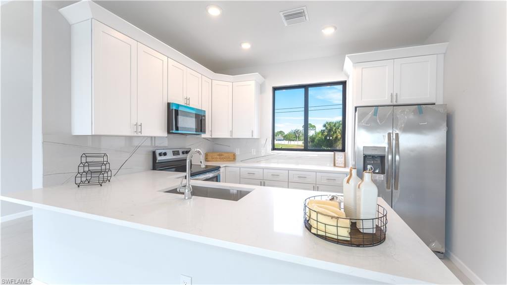 Kitchen featuring appliances with stainless steel finishes, kitchen peninsula, white cabinets, backsplash, and sink