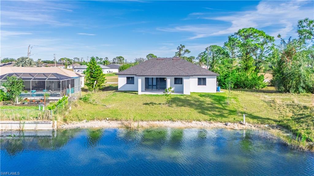 Back of property featuring glass enclosure, a yard, and a water view