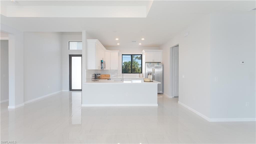 Kitchen featuring an island with sink, stainless steel refrigerator with ice dispenser, backsplash, white cabinetry, and sink