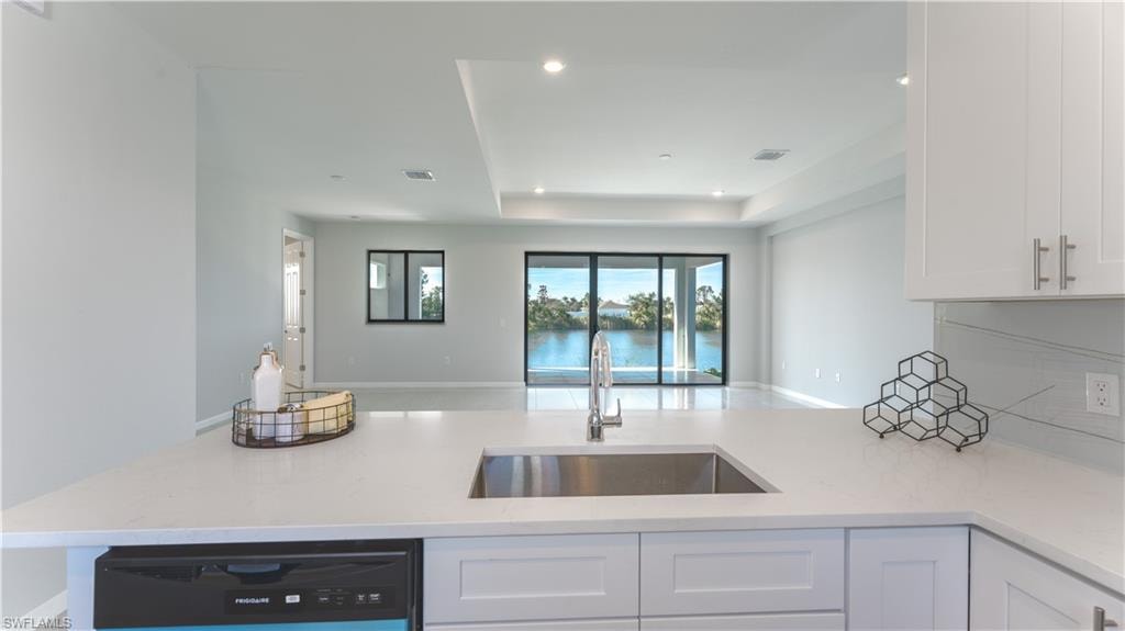 Kitchen featuring light stone counters, a raised ceiling, dishwashing machine, white cabinets, and sink