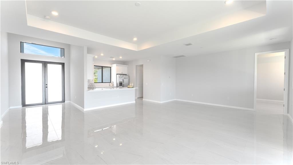 Unfurnished living room with sink, french doors, and a tray ceiling