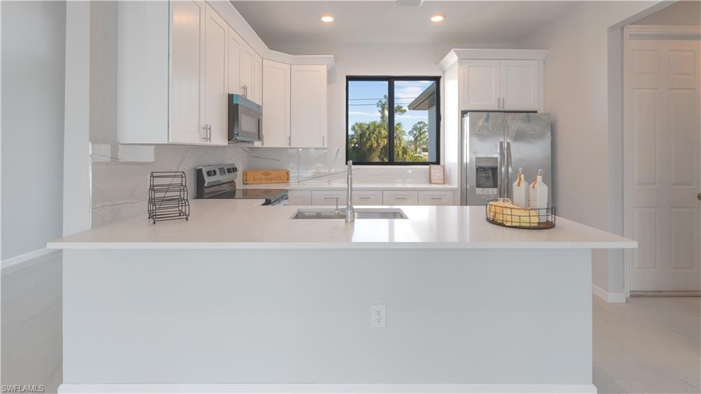 Kitchen featuring kitchen peninsula, appliances with stainless steel finishes, white cabinetry, and sink