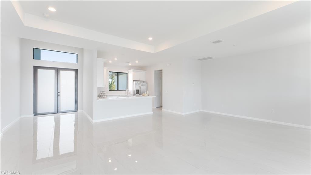 Unfurnished living room featuring sink, french doors, and a tray ceiling