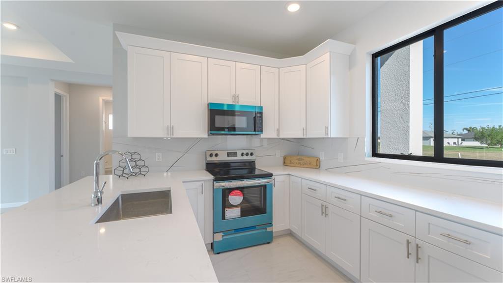 Kitchen with sink, white cabinets, electric range, and tasteful backsplash