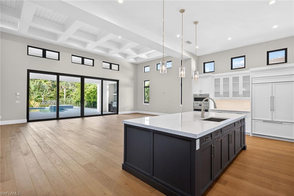 Dual tone kitchen with two tone color scheme, hanging light fixtures, glass insert cabinets, a center island with sink, and open floor plan