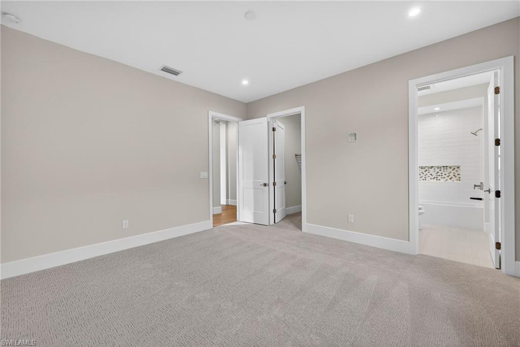 Bedroom 1 with a spacious closet, light colored carpet, recessed lighting, and ensuite bath