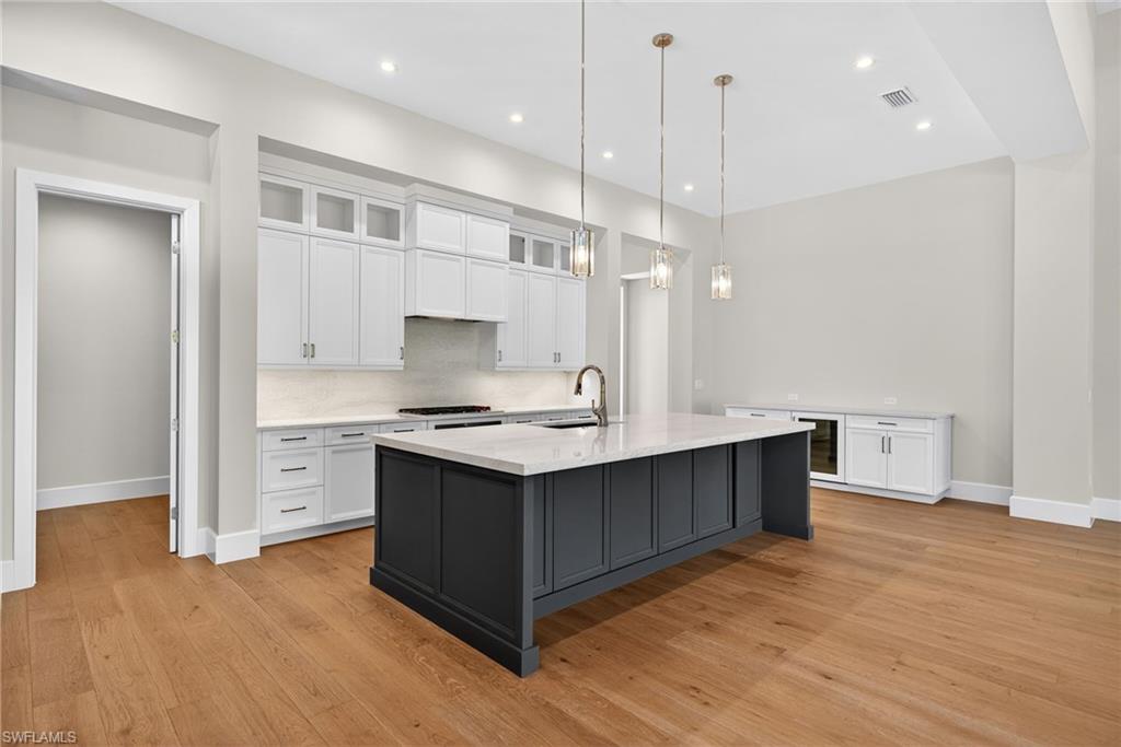 Kitchen with glass insert cabinets, white custom cabinets, elegant and simple hanging light fixtures, large kitchen breakfast bar