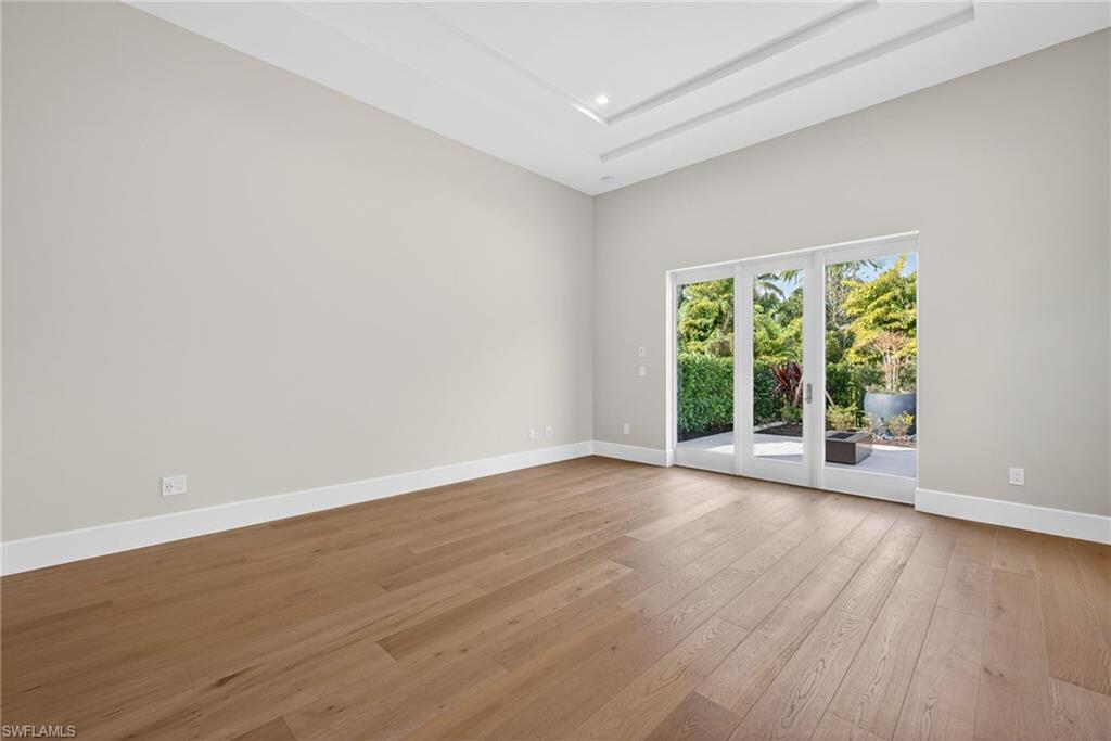 This primary bedroom featuring light wood flooring and a high tray ceiling, French doors leading to private outdoor patio space with fire pit