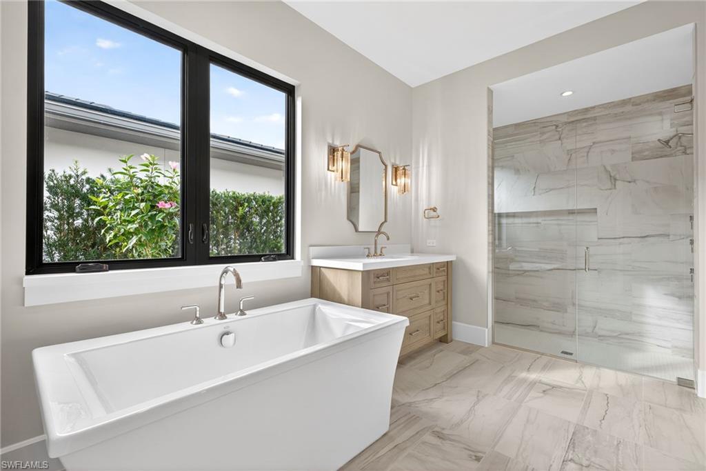 Full bath with light marble finish floors, vanity, a marble finish shower, and a freestanding tub