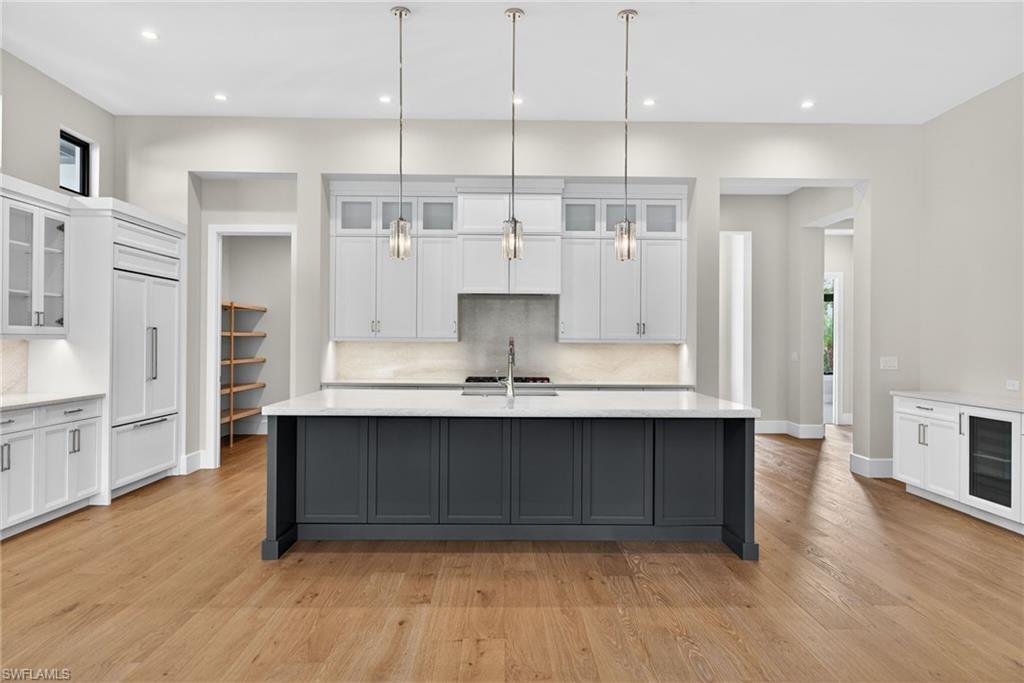 Two tone kitchen featuring glass fronted cabinets, two tone cabinetry, pendant lighting, decorative backsplash, and a large island