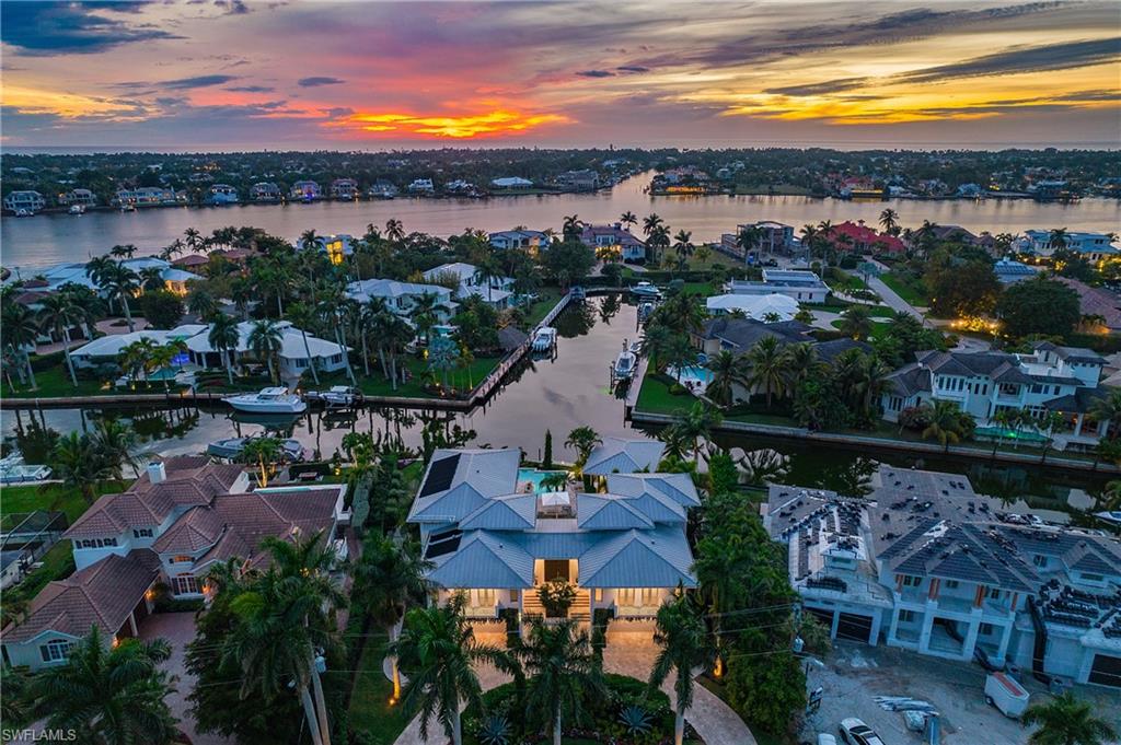 Waterfront estate showcasing a striking metal roof, illuminated façade, and lush tropical landscaping with mature palms