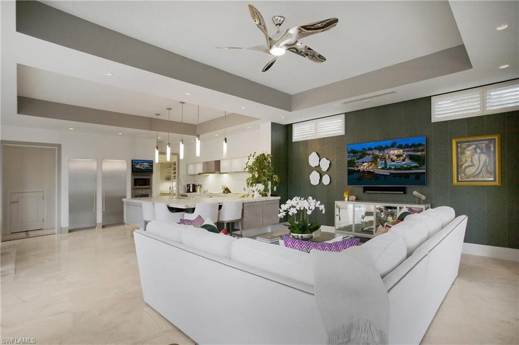 Open-concept living space featuring a curved white sectional sofa, polished concrete flooring, and a coffered ceiling with integrated recessed lighting and ceiling fan