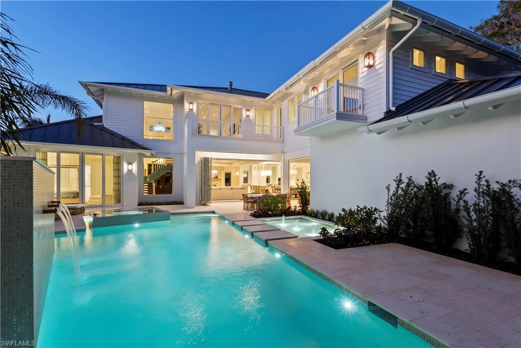 Back house at dusk featuring a pool with hot tub, a patio area, and a balcony
