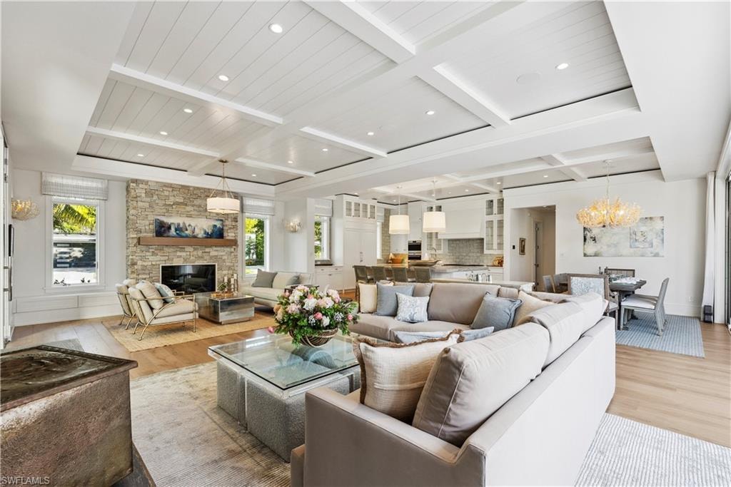 Living room featuring coffered ceiling, a stone fireplace, light hardwood / wood-style flooring, a notable chandelier, and beam ceiling