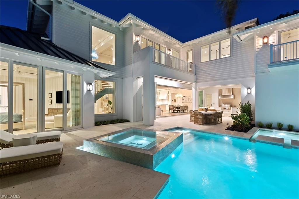 Back house at twilight featuring a pool with hot tub, a patio, and a balcony