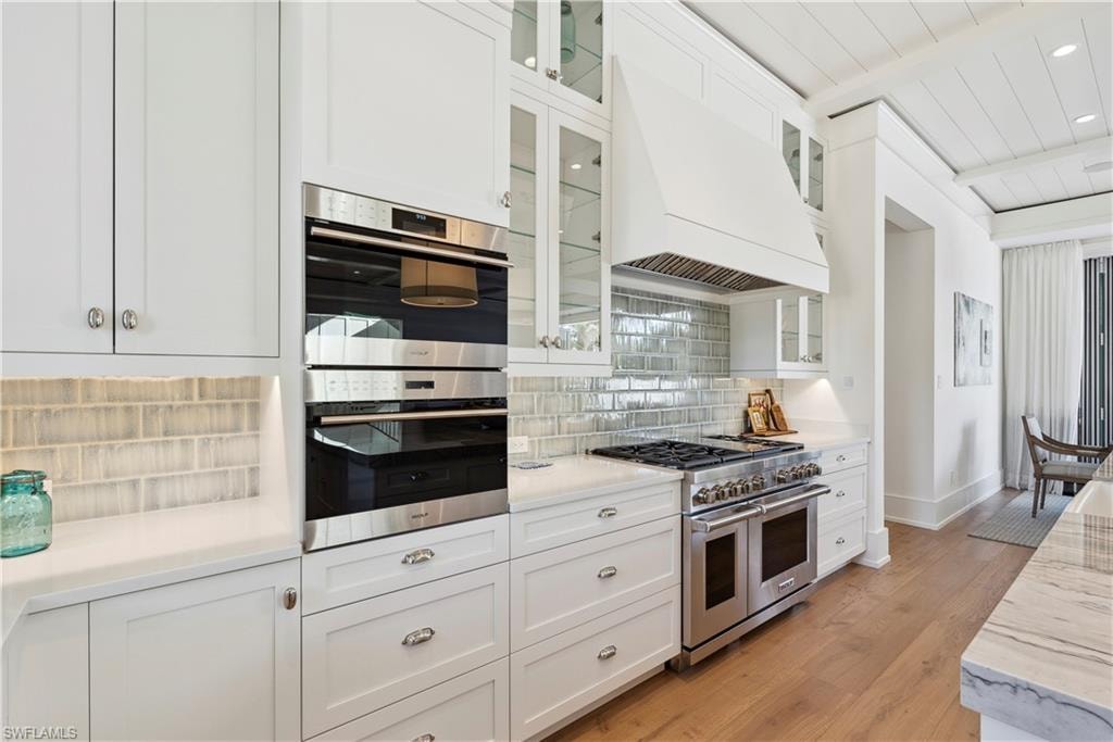 Kitchen featuring white cabinetry, tasteful backsplash, stainless steel appliances, and custom range hood
